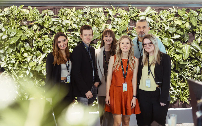 Sechs lächelnde Teammitglieder posieren vor einer grünen Pflanzenwand beim dc:connect Event.