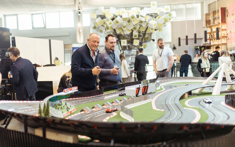 Zwei Männer spielen lächelnd an einer großen Carrera-Rennbahn auf einem dc:connect Event.