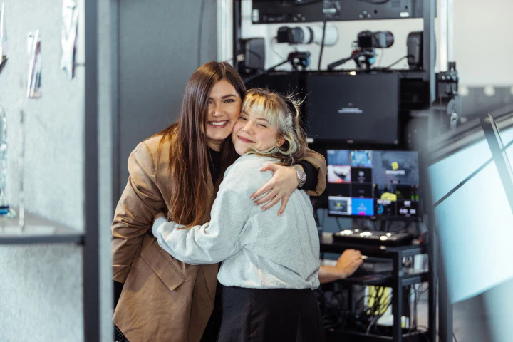 Zwei lächelnde Frauen umarmen sich herzlich vor Technik-Equipment bei einem Jahreskickoff-Event der dc AG.