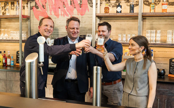 CEO Tobias Langmeyer, Oberbürgermeister Ingo Lehmann, Partner Michael Feuerstein und Vorstand Kristina Langmeyer stoßen mit frisch gezapftem Bier an der Bar auf das neue Office von dc an.