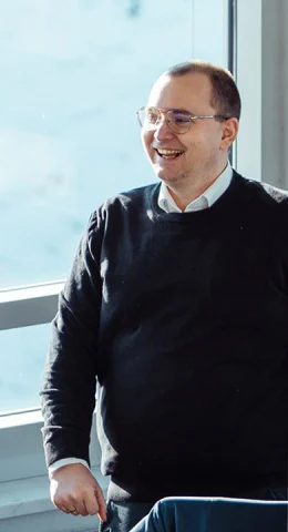 Lächelnder Digitalberater Jörg steht vor einem hellen Fenster im Büro.