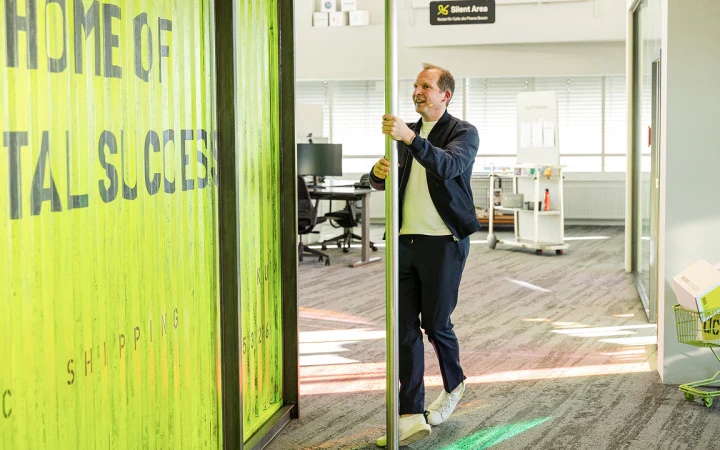 CEO Tobias Langmeyer rutscht lachend eine Feuerwehrstange im modernen Office von dc hinunter.