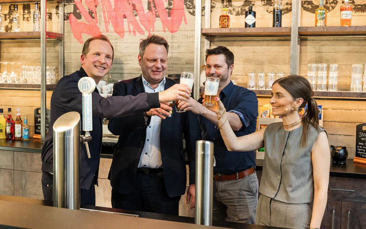 CEO Tobias Langmeyer, Oberbürgermeister Ingo Lehmann, Partner Michael Feuerstein und Vorstand Kristina Langmeyer stoßen mit frisch gezapftem Bier an der Bar auf das neue Office von dc an.