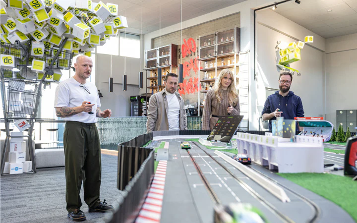 Vier Personen spielen gemeinsam an einer großen Carrera-Rennbahn im Office von dc.