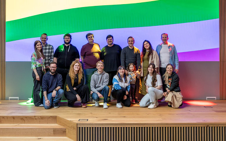 Lächelndes divers zusammengesetztes Team posiert vor einer LED-Wand mit bunten Regenbogenfarben.