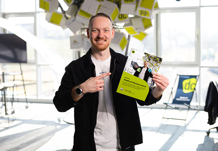 Lukas hält lächelnd ein Whitepaper über Shopify und Business Central von der dc AG in die Kamera.