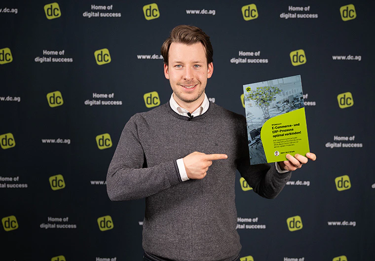 Henri Engels hält ein Whitepaper zu E-Commerce- und ERP-Prozessen von dc vor einer Logowand.