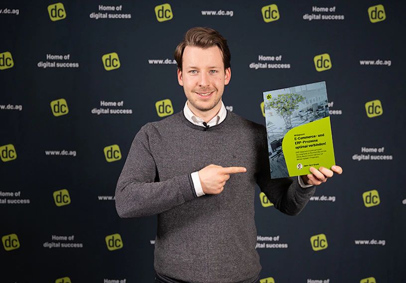 Henri Engels hält ein Whitepaper zu E-Commerce- und ERP-Prozessen von dc vor einer Logowand.
