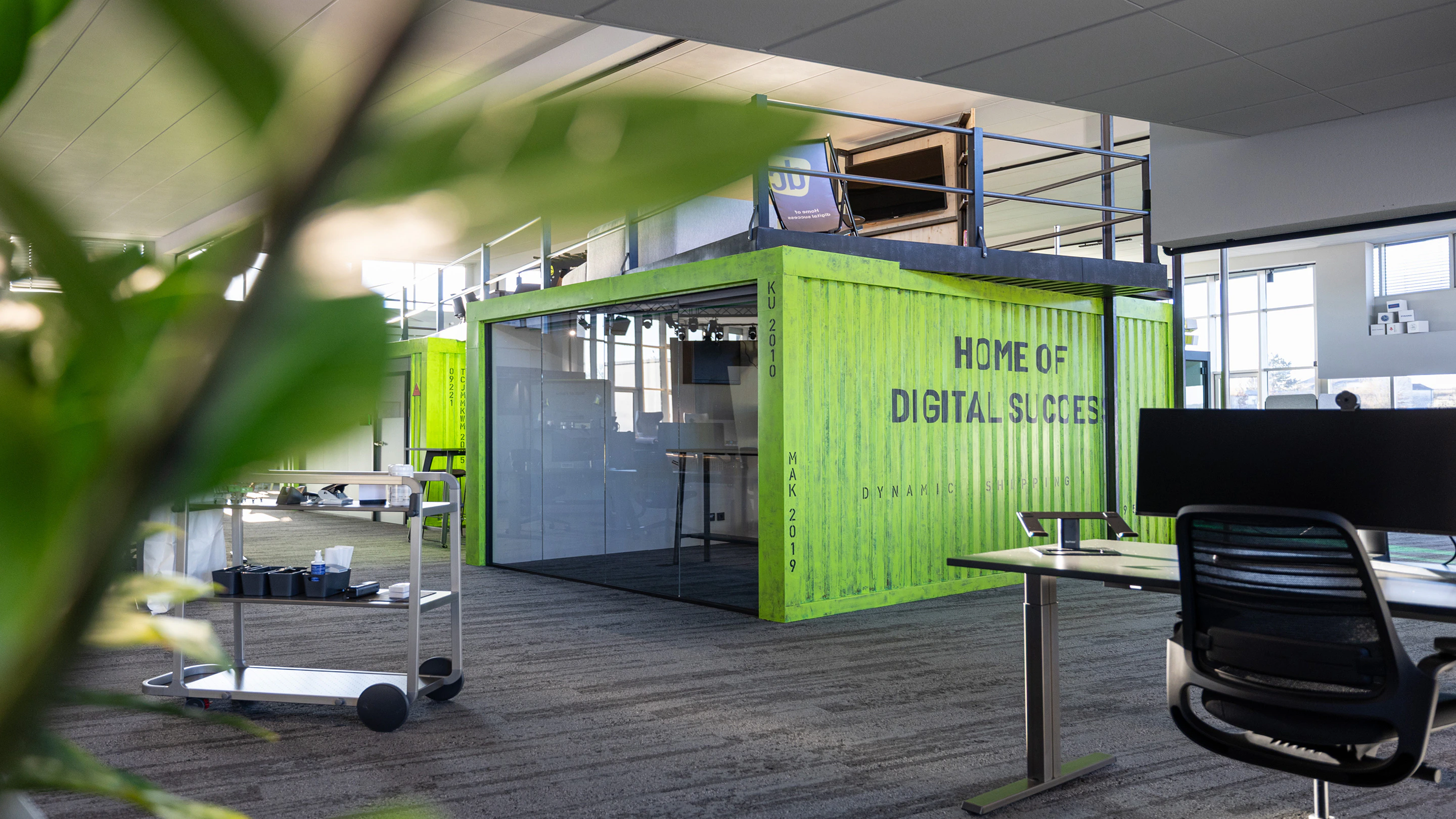 Modernes Großraumbüro mit einem grünen Schiffscontainer als Meetingraum und Aufschrift Home of Digital Success.
