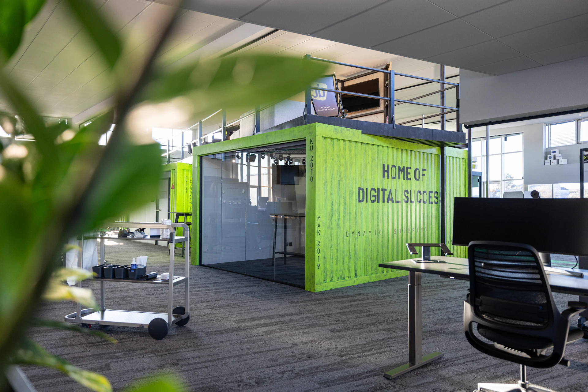 Moderner Büroraum mit einem grünen Container als Meetingraum und dem Text Home of Digital Success.