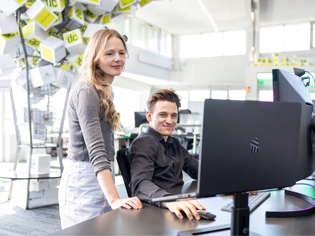 Zwei Kollegen besprechen in einem modernen Büro das Brand Design an einem Apple MacBook.