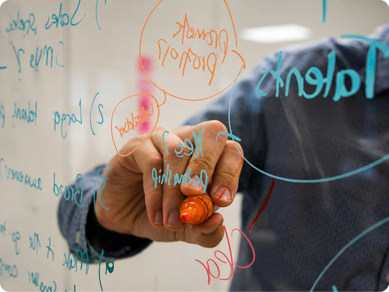 Person skizziert Strategien zum Markendesign und Corporate Wording auf einer Glasscheibe.