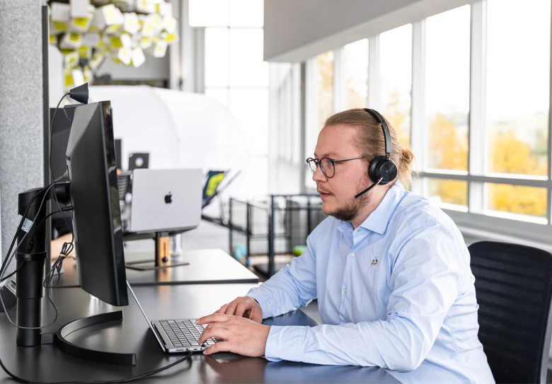 Mann mit Headset arbeitet an einem Microsoft 365 Arbeitsplatz mit Monitor und Laptop.