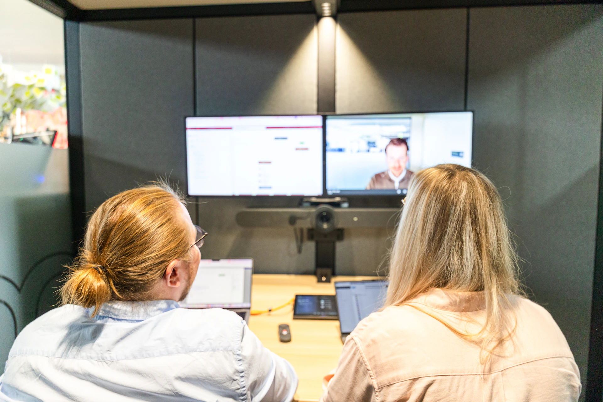 Zwei Personen sitzen vor zwei Monitoren in einer Videokonferenz über Microsoft Teams.