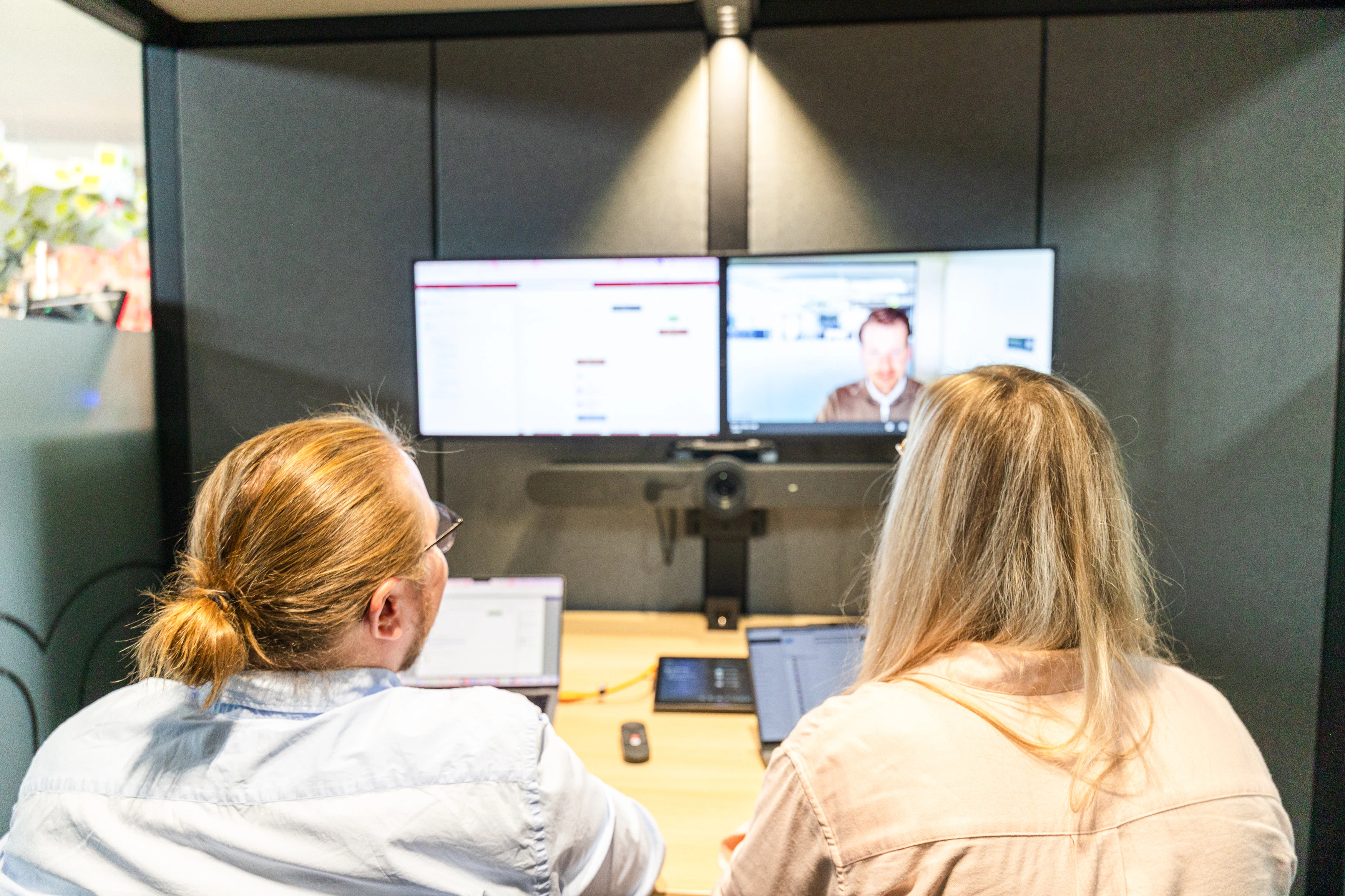 Zwei Personen sitzen vor zwei Monitoren in einer Videokonferenz über Microsoft Teams.