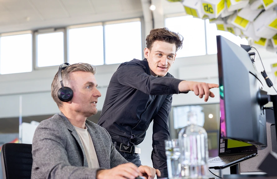 Zwei Kollegen schauen gemeinsam auf Monitor im dc-Büro, einer zeigt auf den Bildschirm