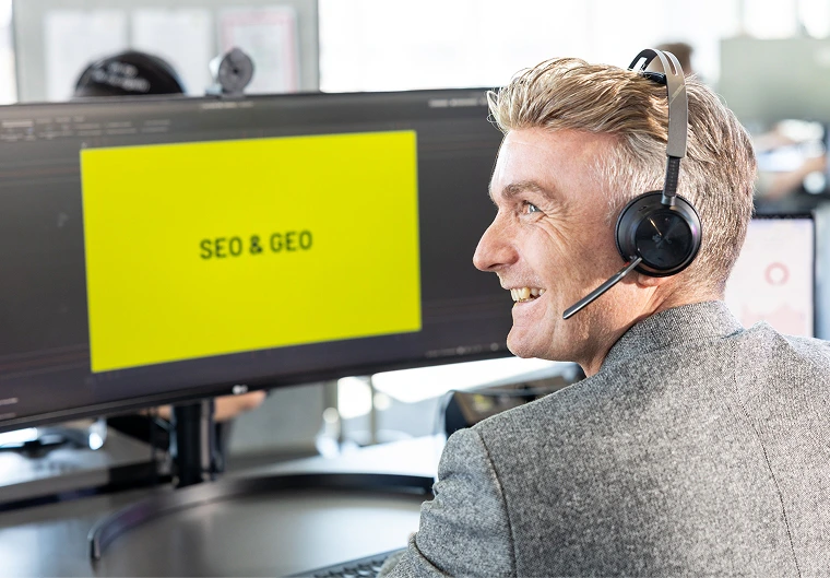 Lächelnder Mann mit Headset vor Monitor mit gelber SEO & GEO Präsentation im Büro