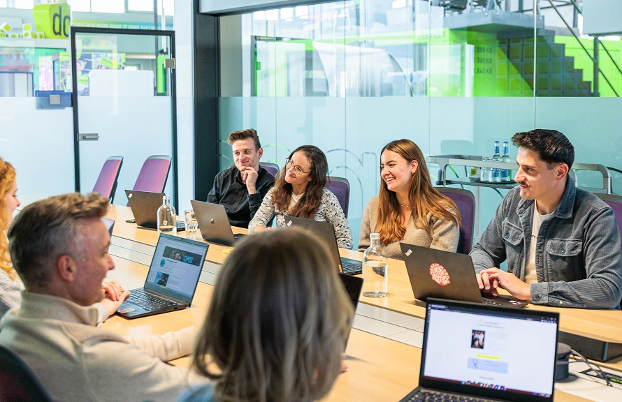 Sechsköpfiges Team beim Meeting mit Laptops in Glaskonferenzraum im dc-Büro