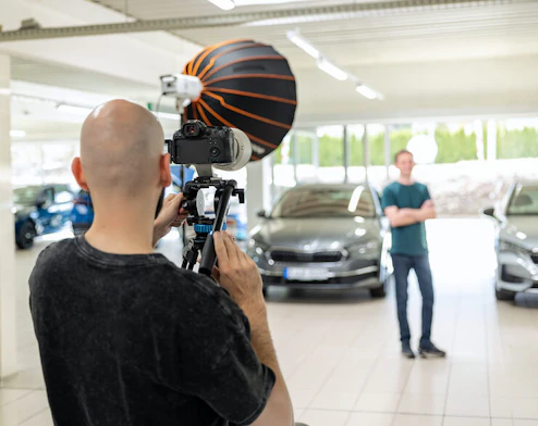 Ein Fotograf fotografiert einen Mann in einem Autohaus mit DSLR-Kamera und aufgebautem Blitz