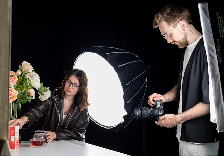 Zwei professionelle Videografen erstellen Aufnahmen eines Produkts im Fotostudio mit DSLR-Kamera und Softbox.