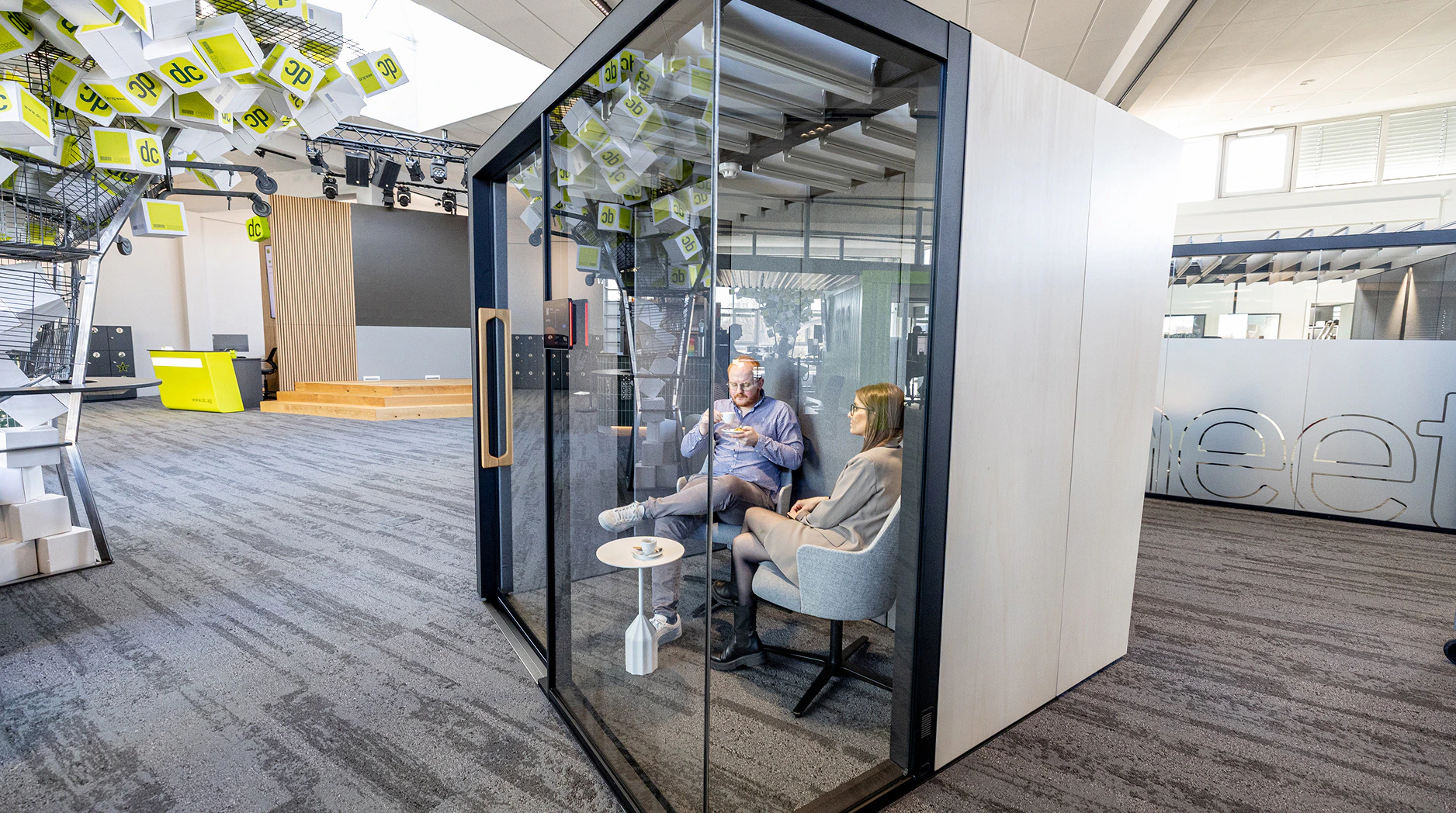 Zwei Personen führen ein Meeting in einer modernen, gläsernen Telefonkabine im Büro.