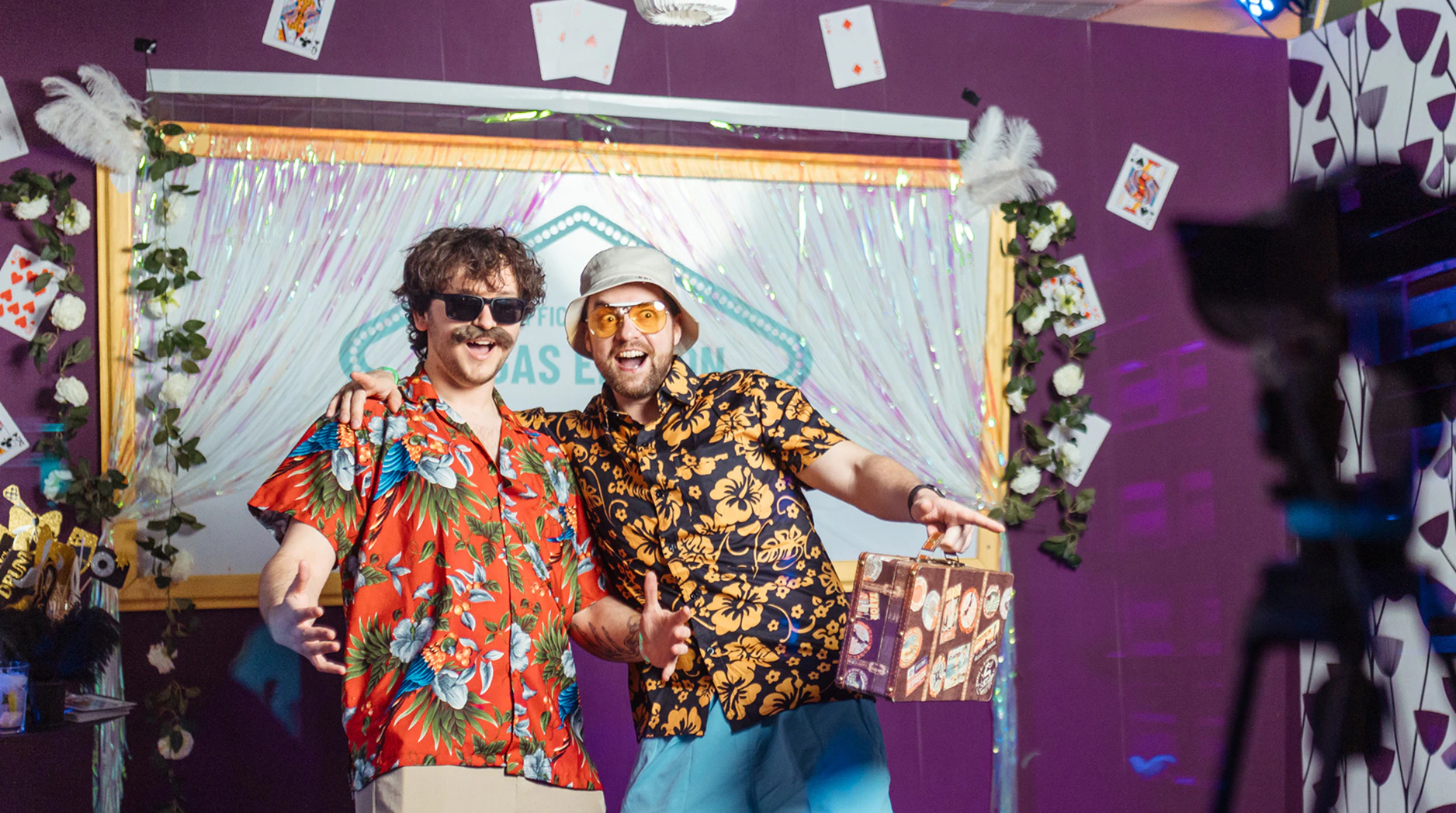 Zwei lachende Männer in bunten Hawaiihemden posieren gut gelaunt bei einer Firmen-Party.