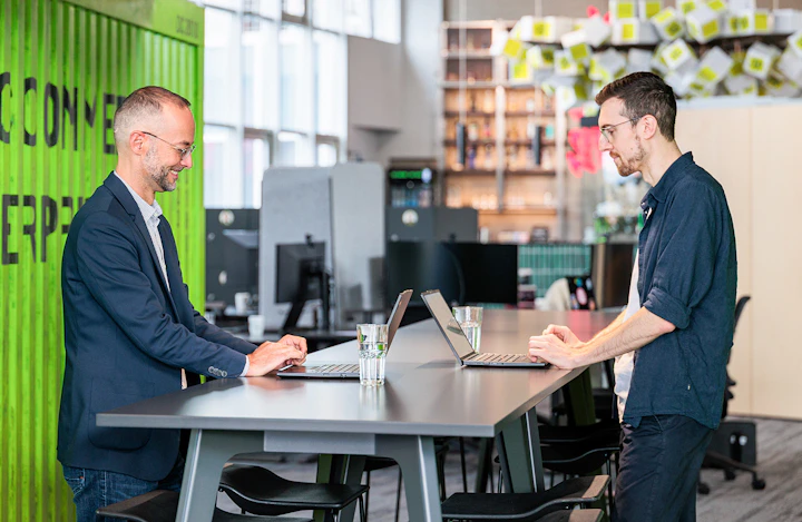 Zwei Männer arbeiten an ihren Laptops an einem modernen Hochtisch in einem Loft-Büro.