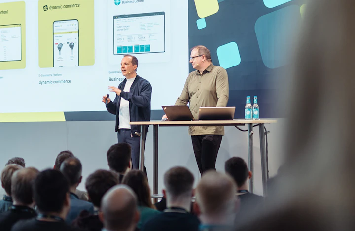 Zwei Experten halten einen Fachvortrag über Digitalberatung und Dynamic Commerce auf einer Bühne vor Publikum.