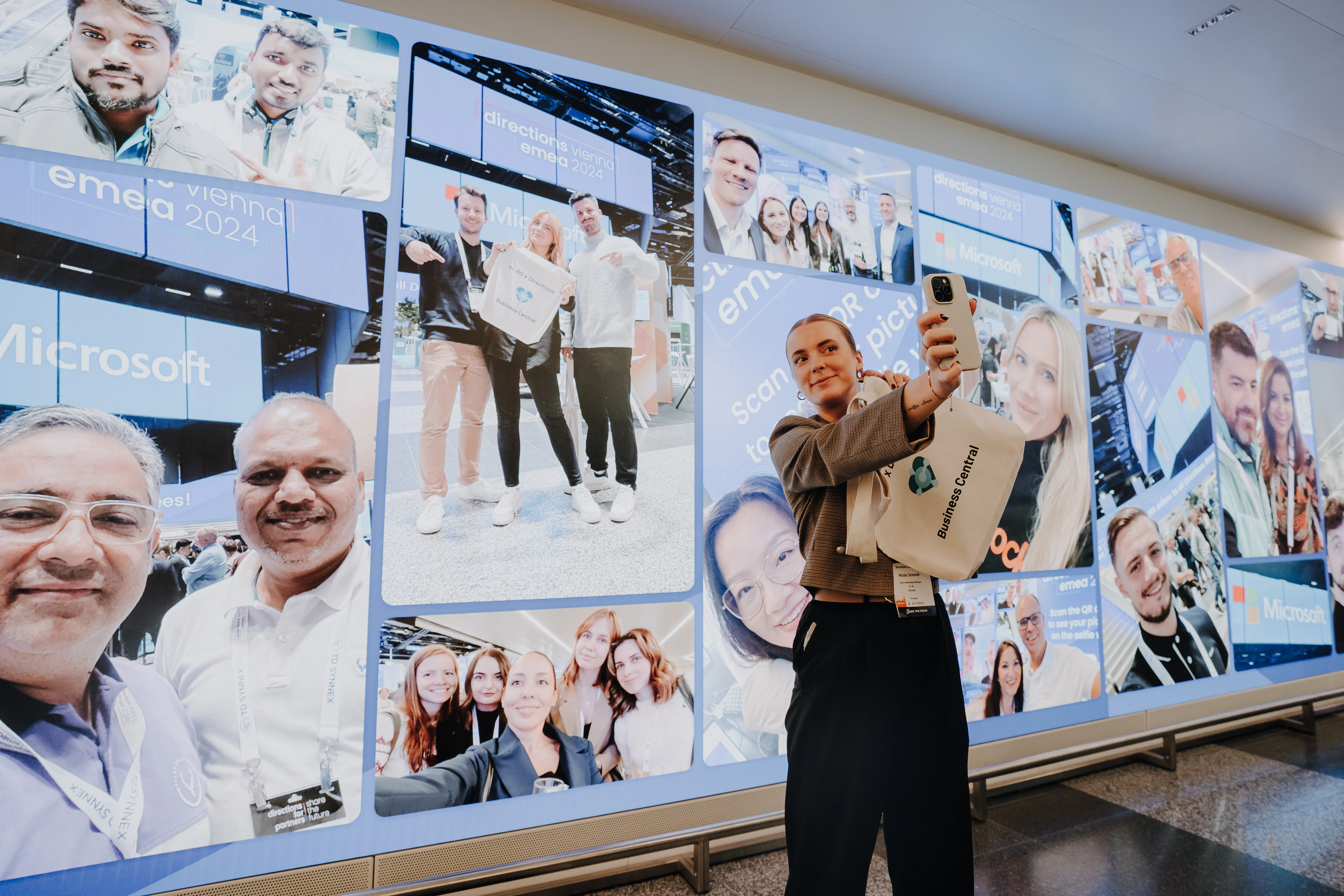 Frau macht ein Selfie vor einer Fotowand der Directions EMEA 2024 mit Microsoft-Logo.