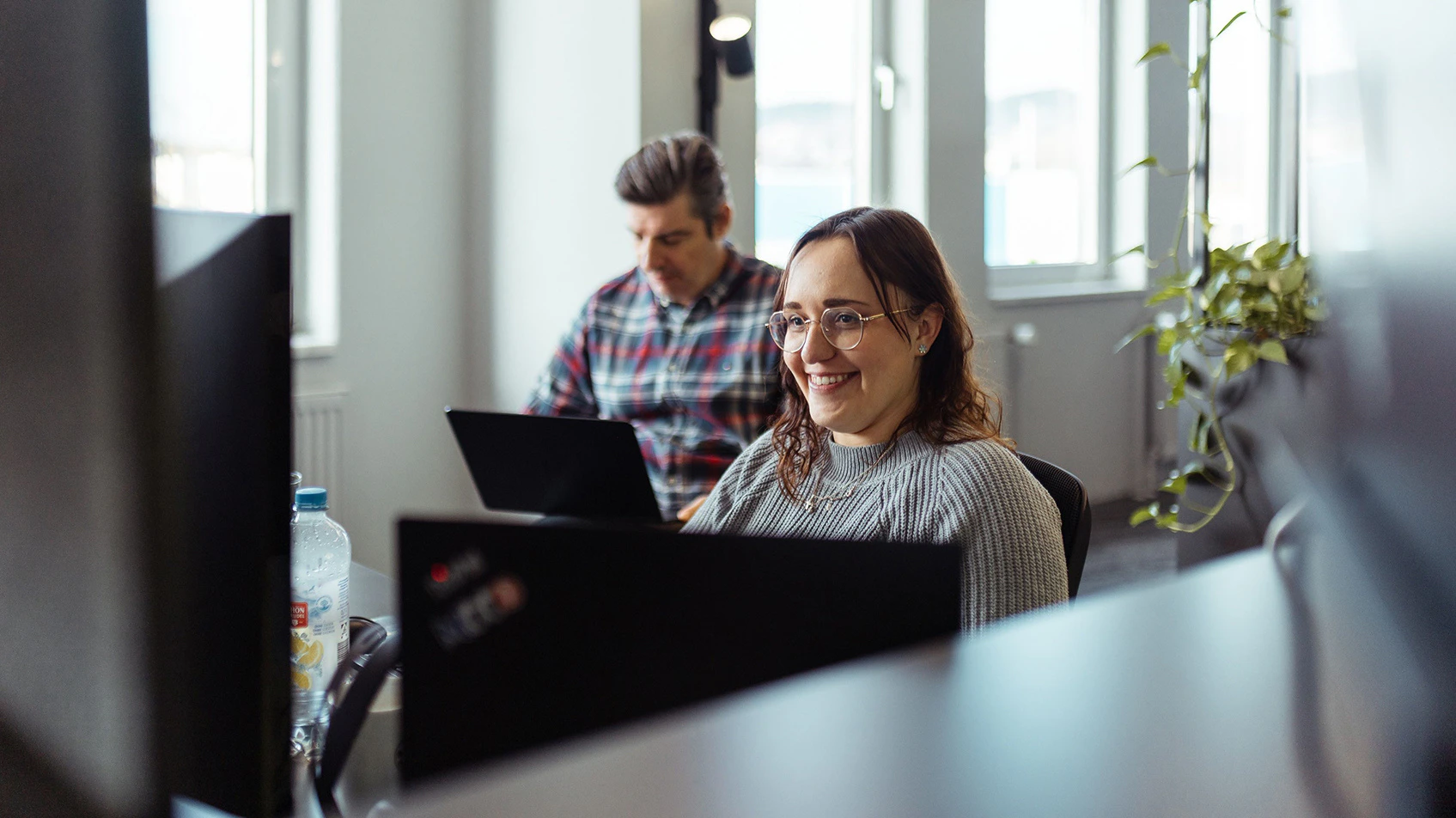 Zwei Consultants arbeiten lächelnd an Lenovo ThinkPad Laptops im modernen dc Office.