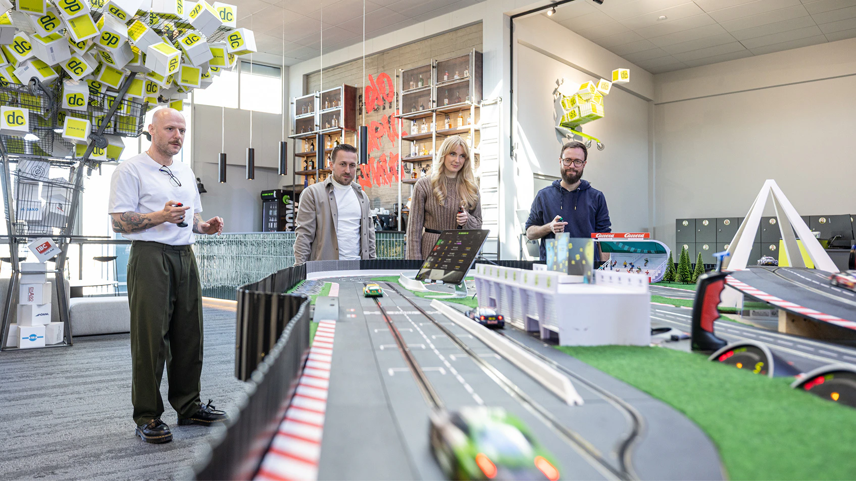 Vier Personen spielen gemeinsam an einer großen Carrera-Autorennbahn im modernen Büro von dc.