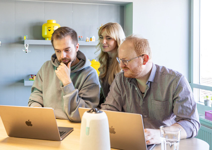 Drei Mitarbeiter einer Digitalagentur arbeiten gemeinsam an Apple MacBooks im Büro.
