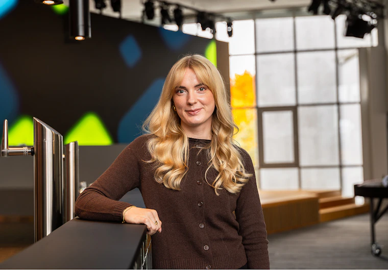Nicole Schmidt in brauner Strickjacke lehnt lächelnd an einer Theke in einem modernen Eventraum