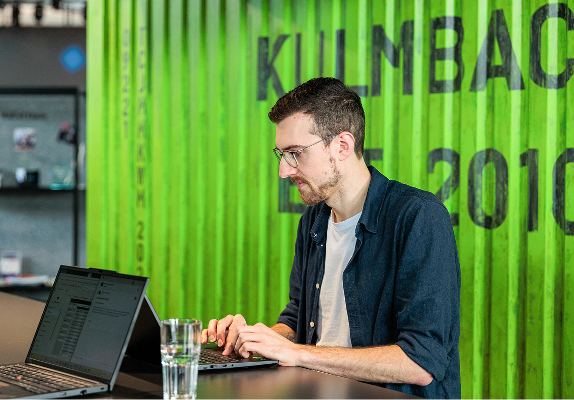 Robin von dc arbeitet konzentriert am Laptop vor einer grünen Containerwand.